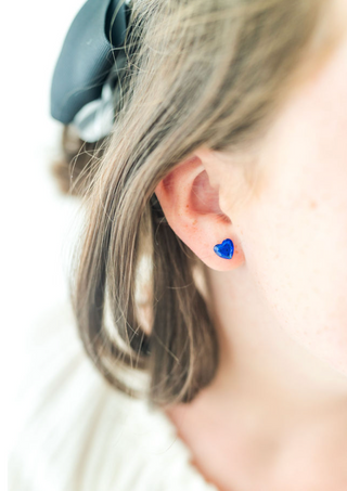 Close-up of an ear wearing a blue heart-shaped earring with a blurred background