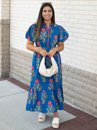 Women in blue dress with pink flowers holding a off white small handbag