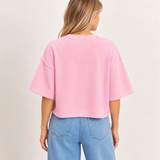 Back view of a pastel pink short sleeve knit sweater featuring a relaxed fit, dropped shoulders, ribbed crew neckline, and straight hem, styled with light-wash denim jeans.