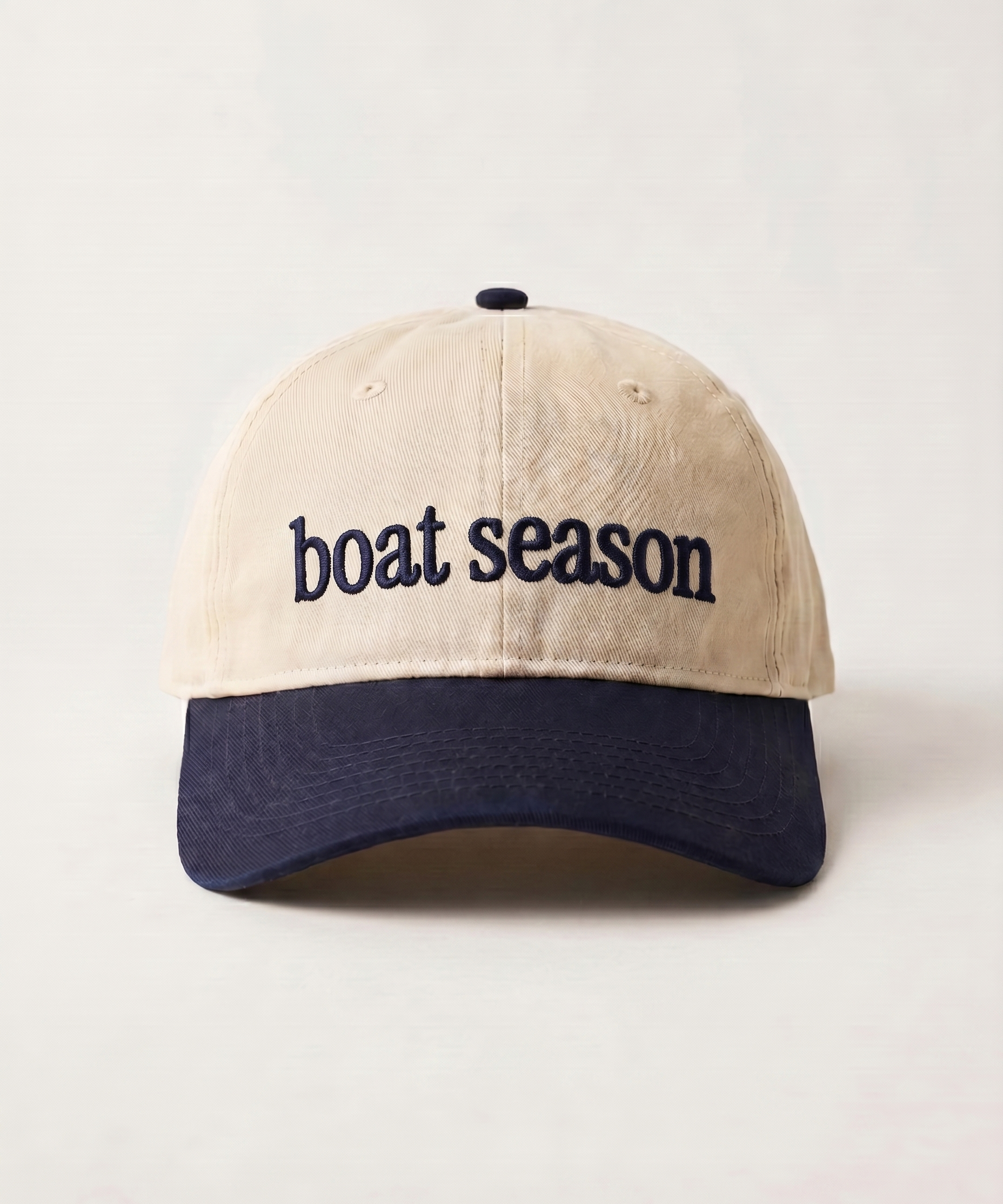 Beige and navy cap with 'boat season' text on a light gray background