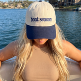 Person wearing a 'boat season' cap by a lake