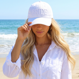 Woman wearing a white cap with 'BRIDE' on it at the beach