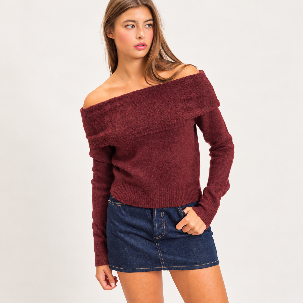 Model wearing the Marlowe burgundy off-shoulder knit sweater with a wide fold-over neckline, long sleeves, and dark denim skirt.