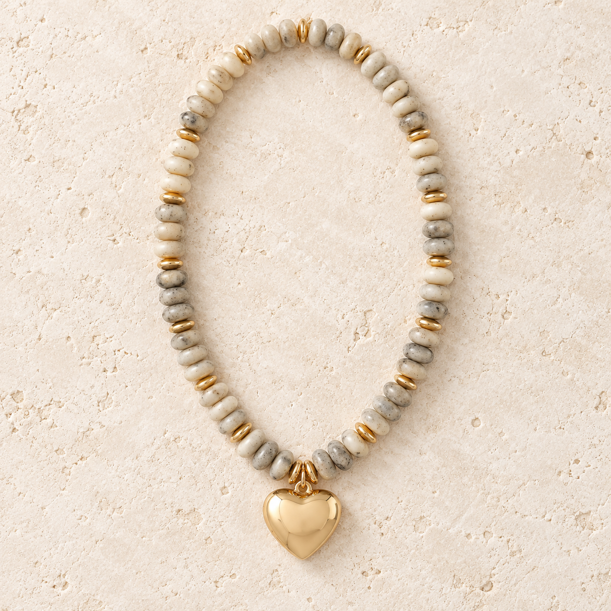 Neutral speckled beaded necklace with gold-tone spacers and heart pendant.