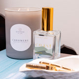 Candle and perfume bottle with 'Cashmere' and 'Coast' labels on a light surface.