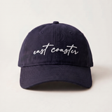 Navy blue cap with 'east coaster' text on a light beige background