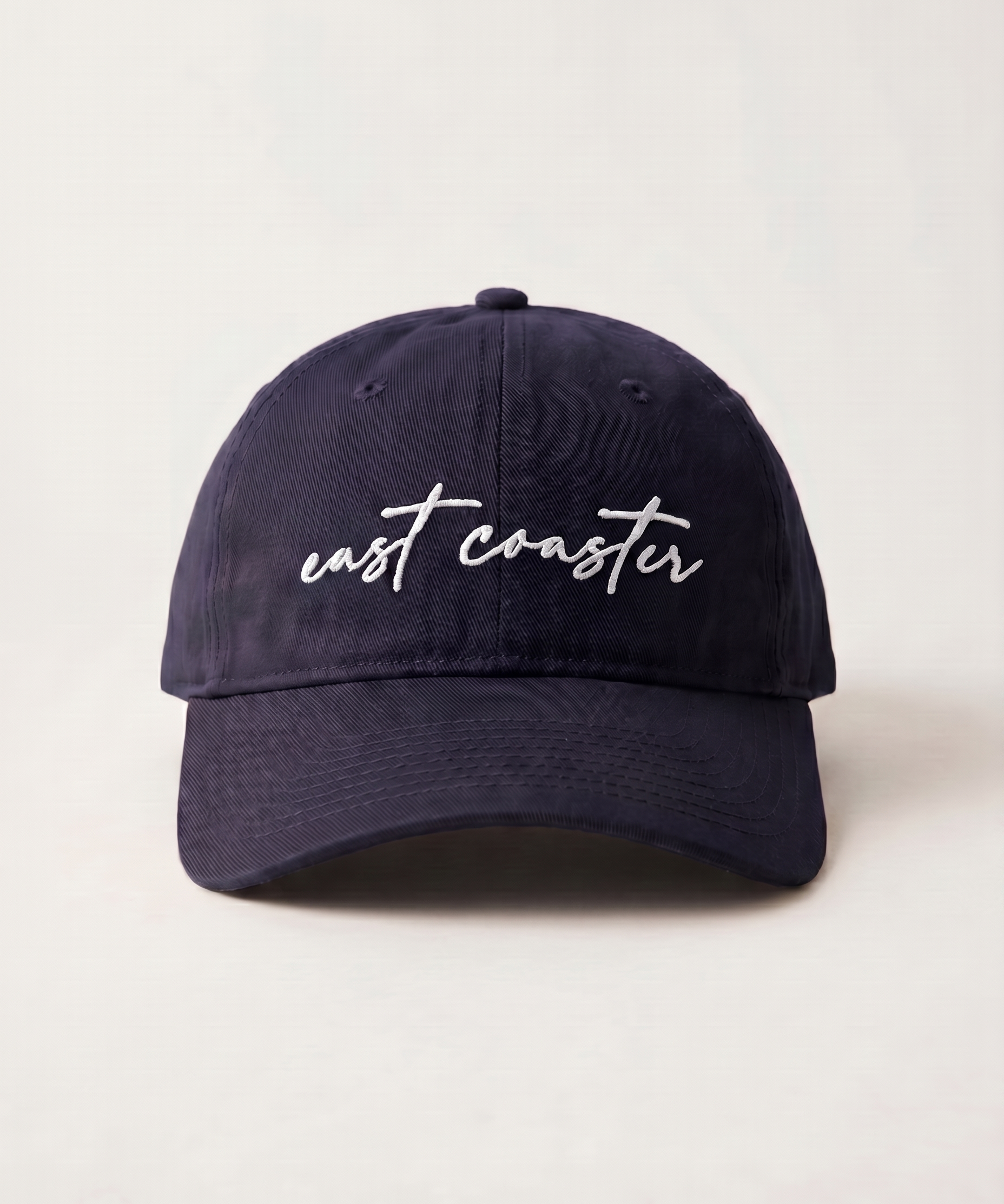 Navy blue cap with 'east coaster' text on a light beige background