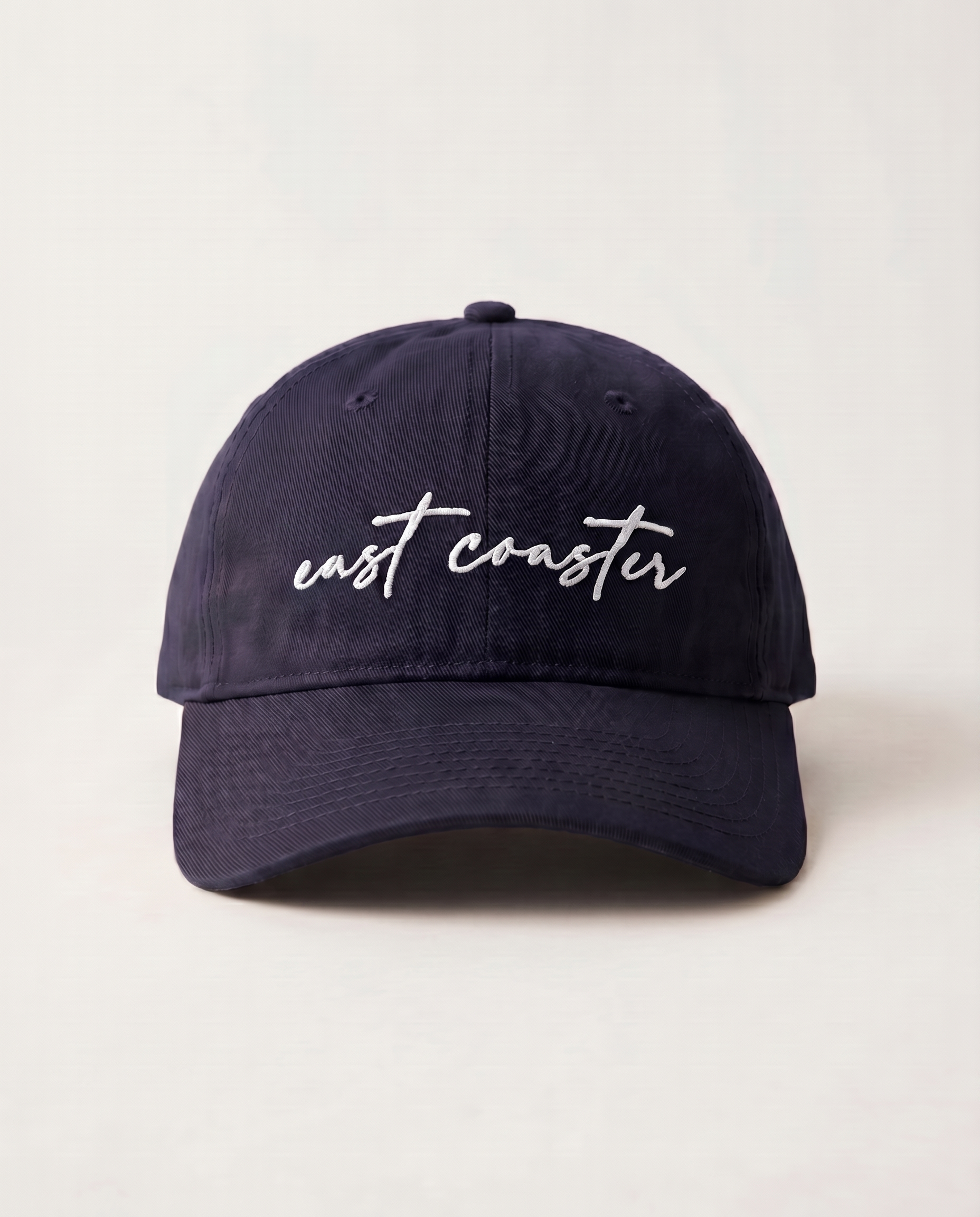 Navy blue cap with 'east coaster' text on a light beige background