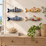 Four hand-painted stoneware fish displayed together on a cream wall above a wood console