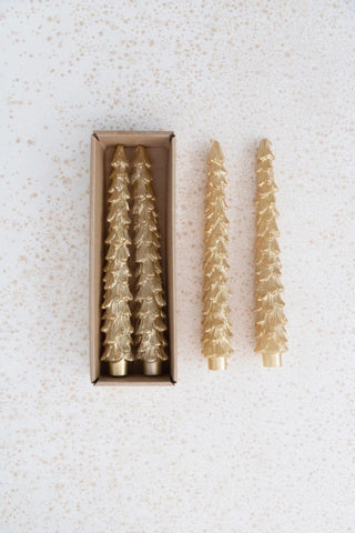 Set of gold Christmas tree-shaped candles with one candle outside its box on a textured white background.
