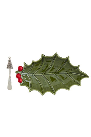 Green ceramic holly leaf with red berries and a silver spoon on a white background