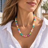 Woman wearing a colorful beaded necklace with gold-tone accents and a white linen blouse.