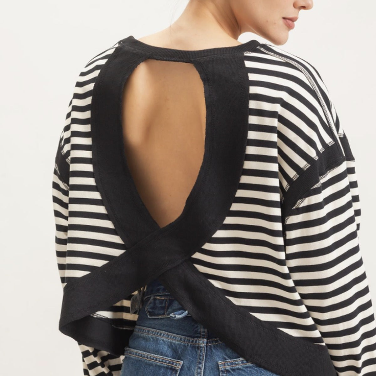 Back view of women's black and cream striped long sleeve top featuring a dramatic open-back design with crisscross fabric detailing.