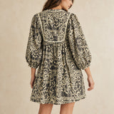 Back view of charcoal and cream botanical cotton peasant dress showing contrasting yoke trim and gathered silhouette.