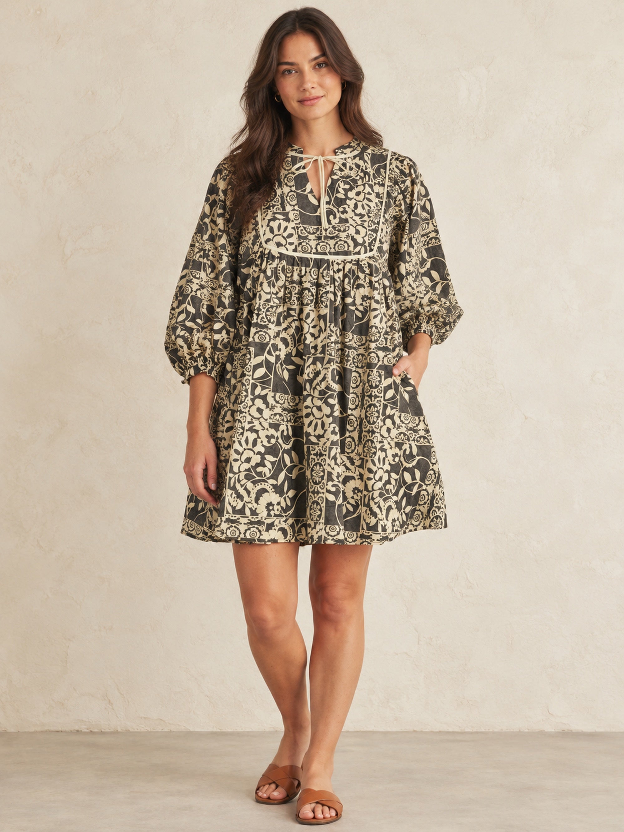 Front view of charcoal and cream floral and leaf print cotton peasant dress with tie neck and three-quarter puff sleeves.