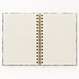 Open floral spiral notebook showing lined cream pages and gold-tone wire binding