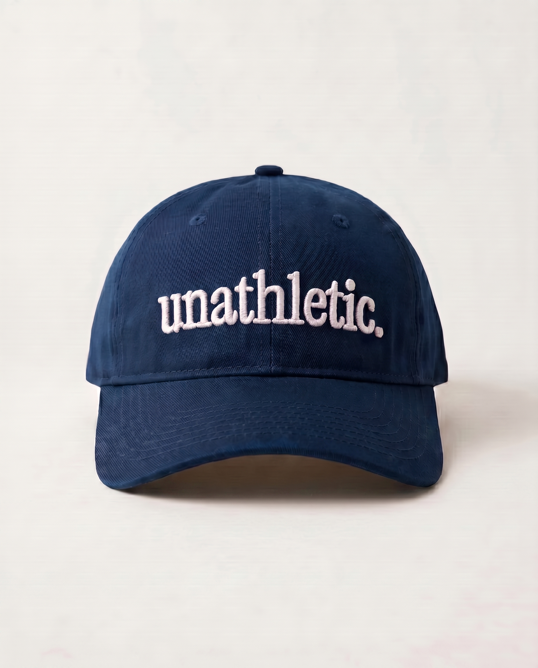Navy blue cap with 'unathletic' text on a light beige background
